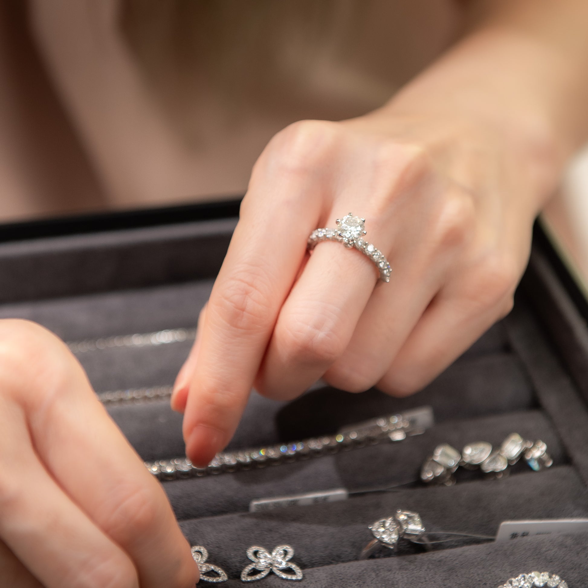 Close-up of hands with a diamond ring over an open jewelry box containing various rings.