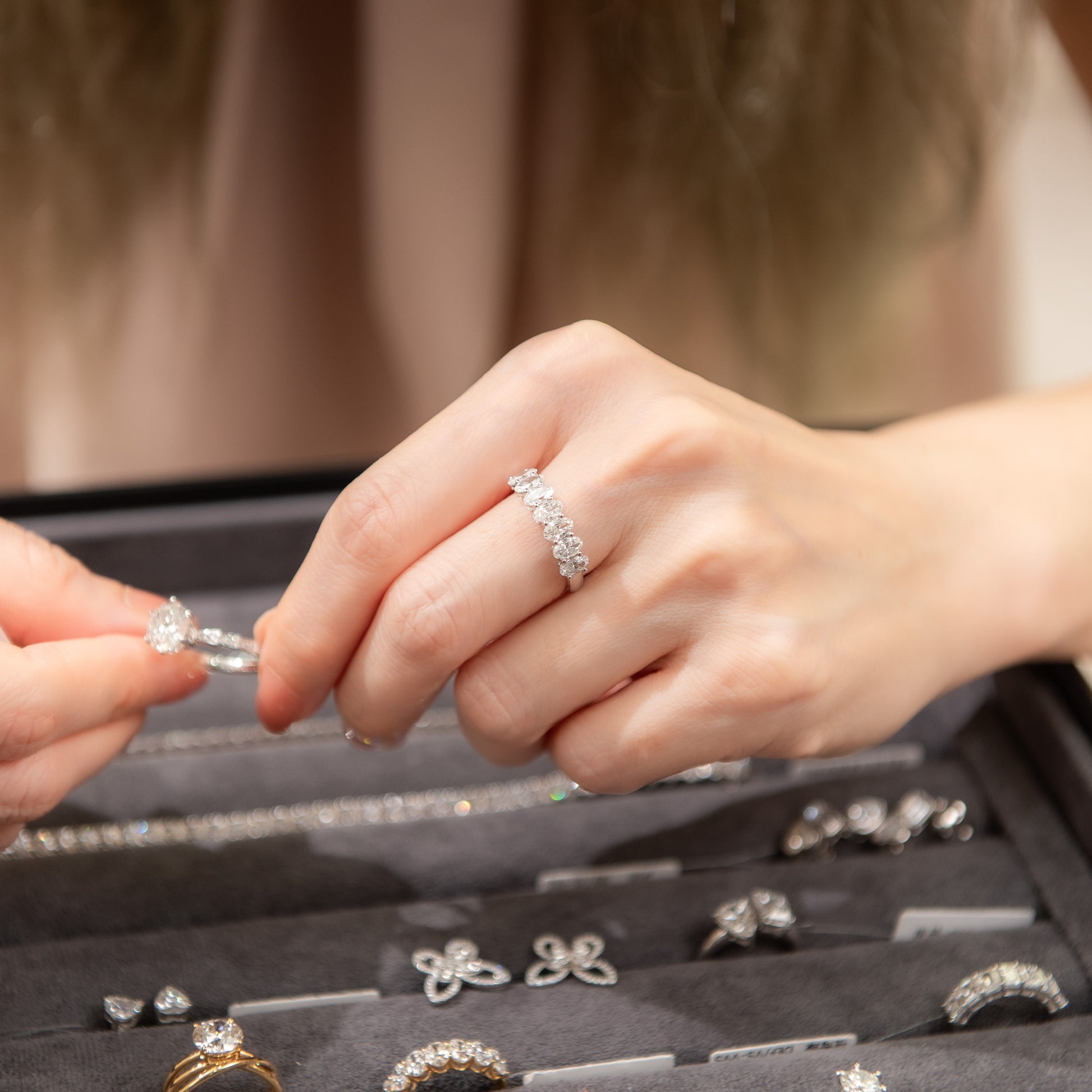 Close-up of hands examining diamond rings with a jewelry box in the background