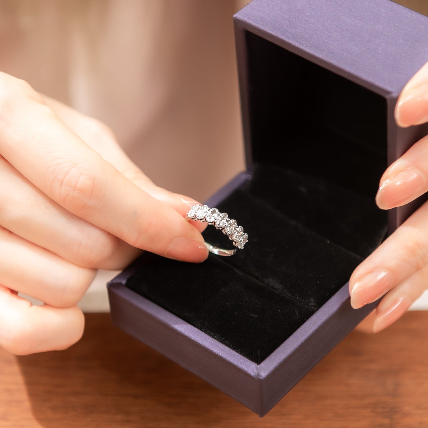 Silver ring being placed into a purple jewelry box by hands.