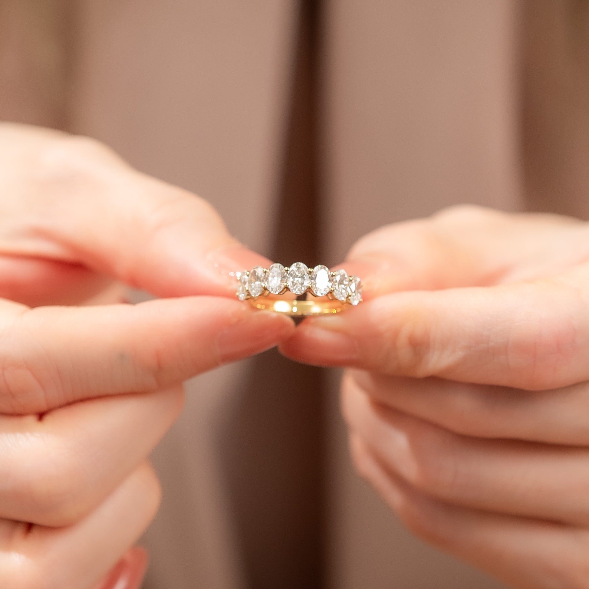 Close-up of hands holding a diamond ring against a neutral background