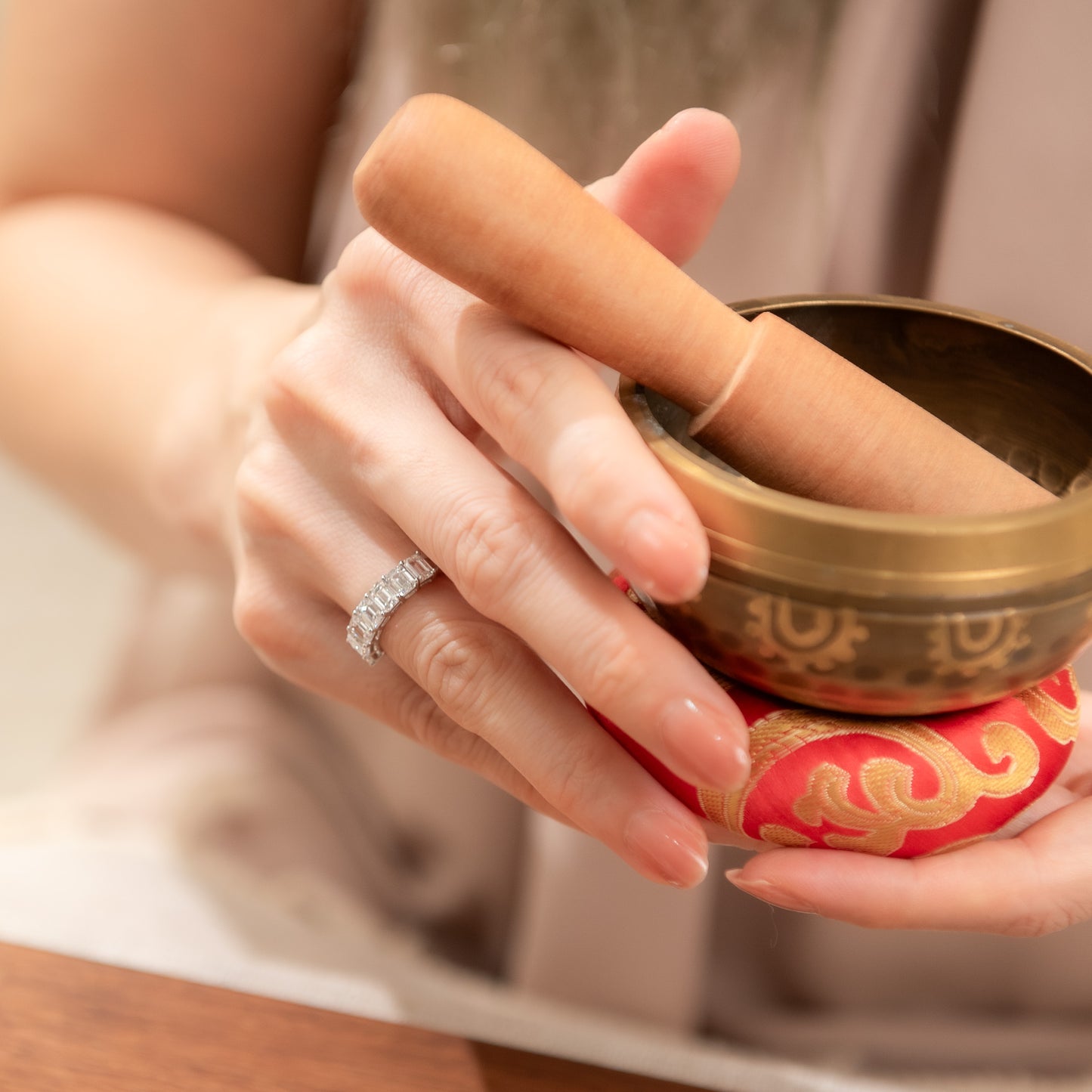 Close-up of hands holding a small brass bowl with a red and gold decorative item.