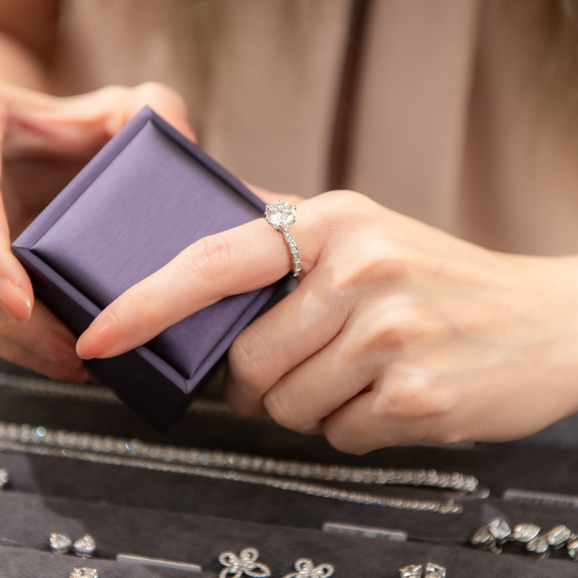 Person holding a purple jewelry box with a ring on a blurred background of jewelry.