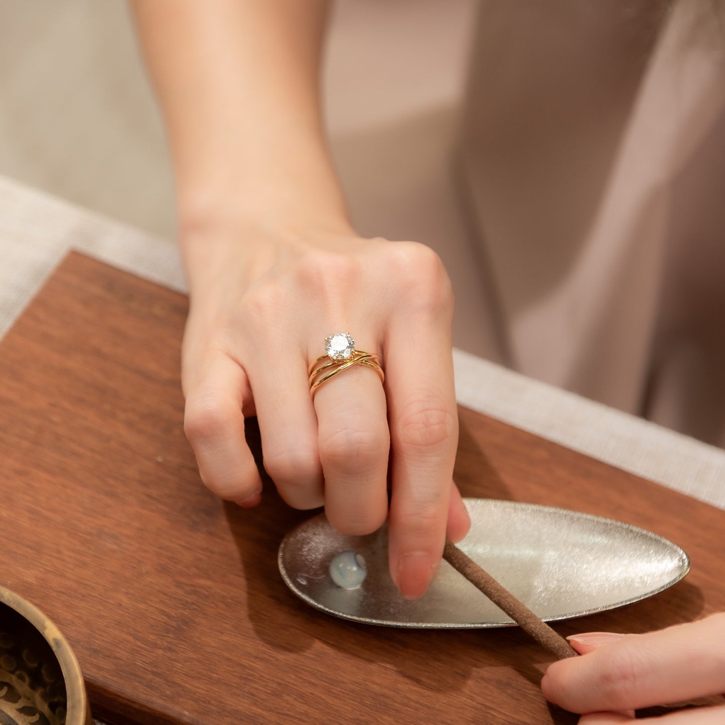 Person lighting an incense stick with a small metal dish on a wooden surface.