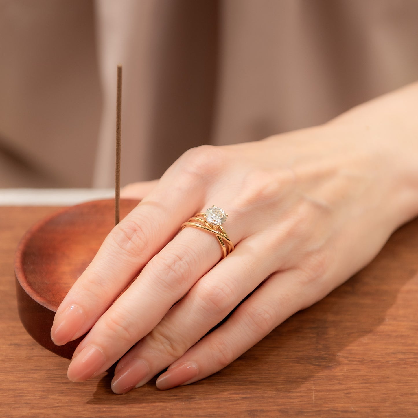 Hand wearing a gold ring with a diamond on a wooden surface