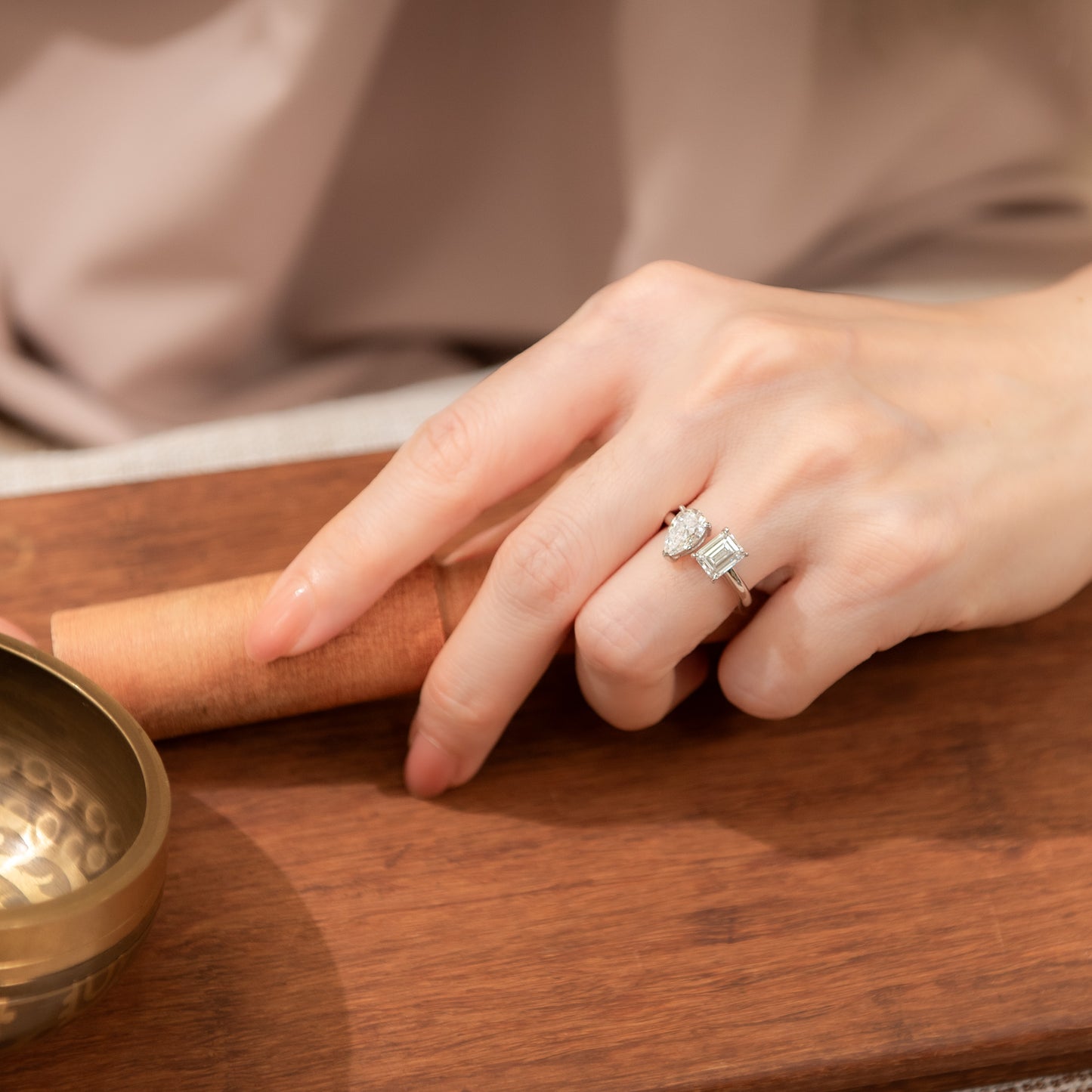 Hand wearing a diamond ring on a wooden surface with a small bowl.
