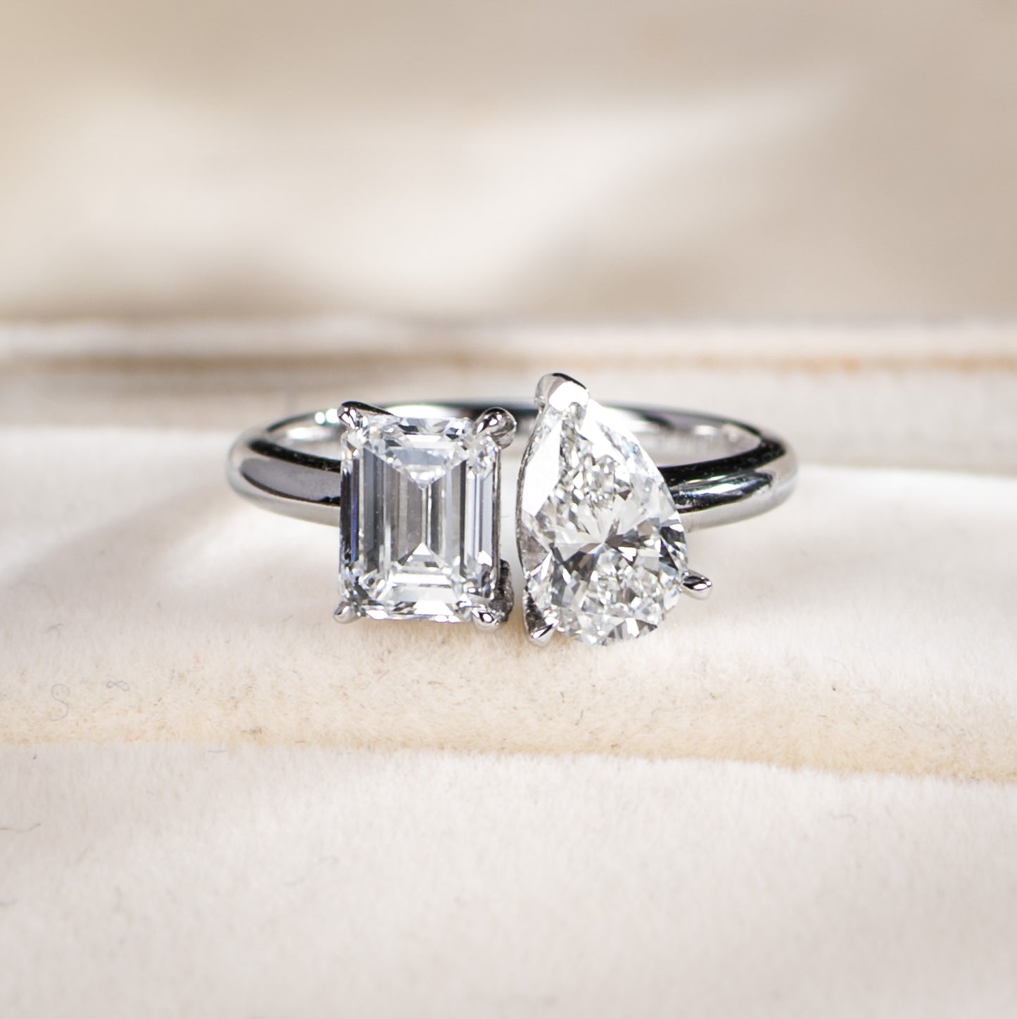 Diamond ring with emerald-cut and pear-shaped gemstones on a soft background