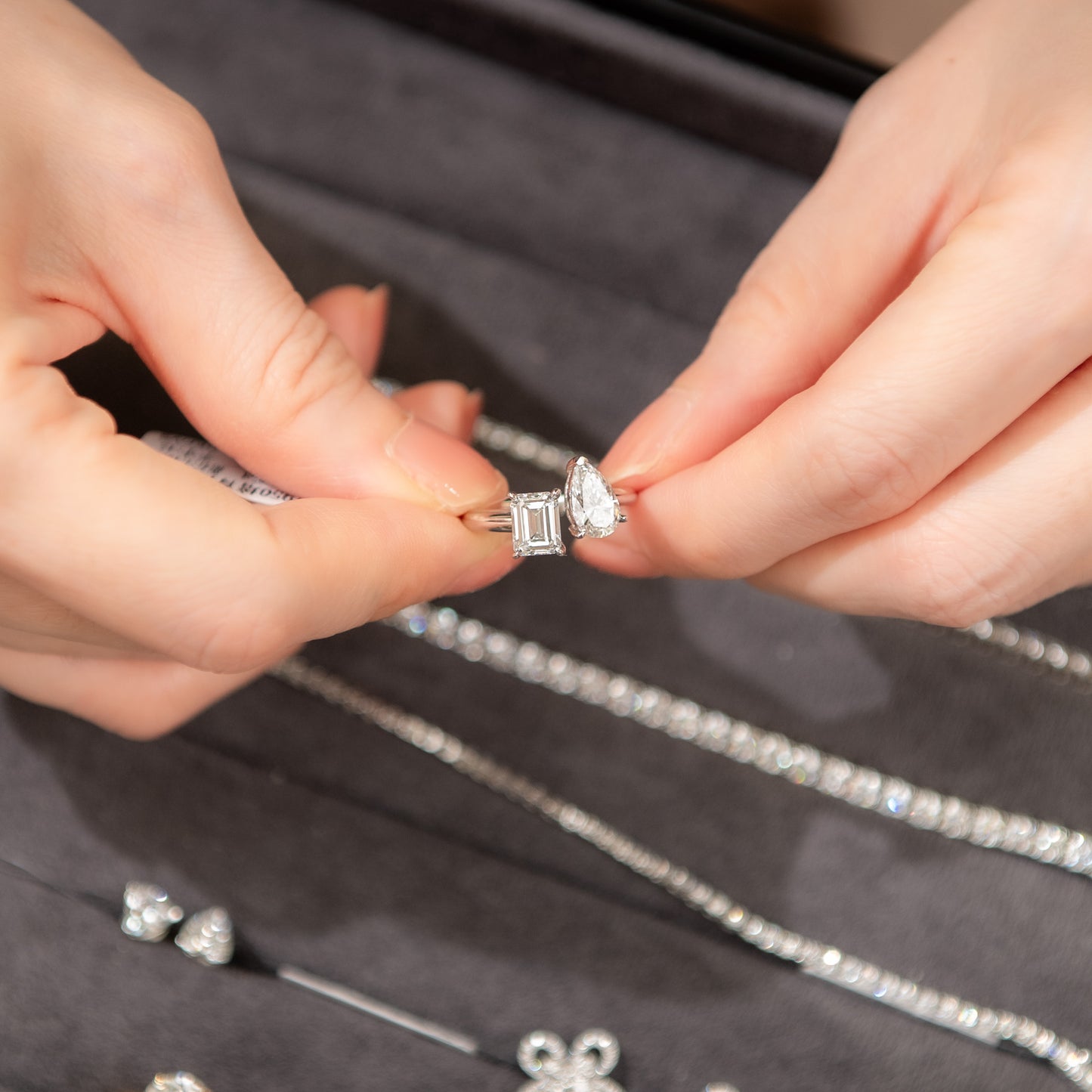 Close-up of hands holding a diamond ring on a dark fabric background