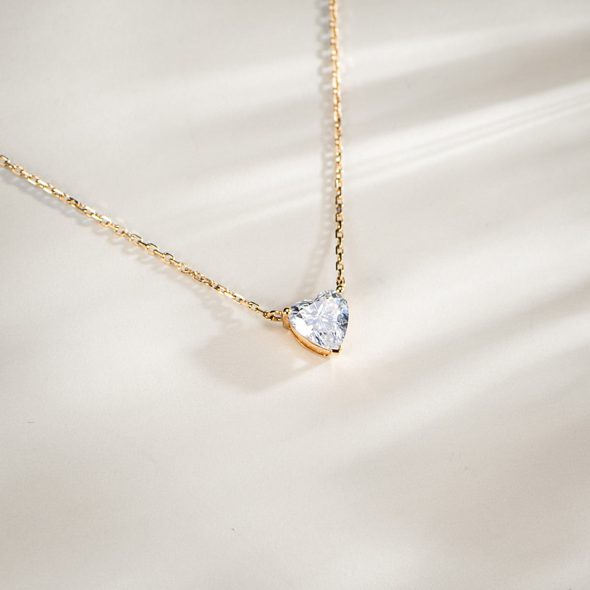 Aurora heart diamond pendant and fine gold chain resting on ivory fabric