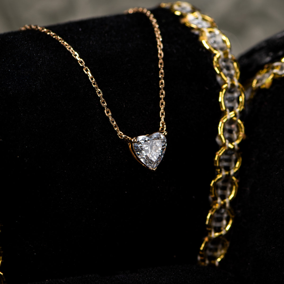 Close-up of the heart-shaped lab-grown diamond pendant on a yellow gold chain against black velvet